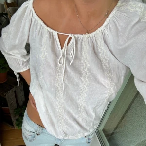 Vit blus med knytband - En vit blus med knytband framtill och broderade detaljer. Blusen har trekvartsärmar och en lös passform💕