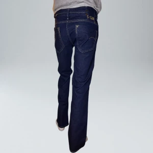 Lågmidjade Vintage Bootcut Jeans  - VARAN KAN KÖPAS DIREKT PÅ VÅR HEMSIDA, ettmarke.se MÄRKE: G-STAR. MODELL: Lågmidjade & Bootcut. FÄRG: Mörkblå. STORLEK: W31 L32 enligt lapp. Uppskattad storlek 40. MIDJA RAKT ÖVER: 41,5 cm. MIDJEHÖJD: 18,5 cm. TOTALLÄNGD (FRÅN MIDJAN): 98 cm. 