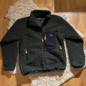 Patagonia Fleece Jacket - Presenting a military green Patagonia fleece jacket, impeccably maintained at a solid 9/10 condition. This rugged yet stylish outerwear piece not only delivers reliable warmth but also adds a touch of adventurous flair to your wardrobe. 