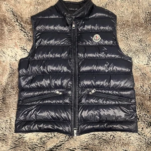 Moncler GUI väst  - Moncler gui väst i storlek 2. Ny pris är 8400. Köpt på Moncler med kvitto. Knappt använd då jag växte ur den efter en vår. Skick 9/10. 