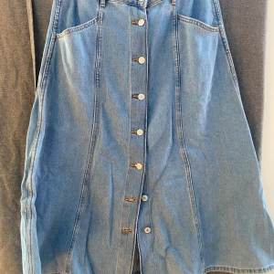 Jeanskjol med knappar fram  - Jeanskjol mer knappar fram. Flickor i sidorna.  Storlek 40 , slutar lite nedanför knät. 