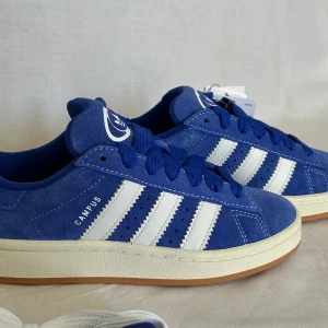 Adidas Campus 00’s ”Lucid Blue💙” - Säljer ett par Adidas Campus 00’s ”Lucid Blue” i storlek 36, HELT NYA. Låda samt blåa och vita skosnören medkommer. Möts i Stockholm samt frakt.