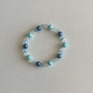 Egengjort pärlarmband  - Ett egengjort pärlarmband med färgerna blå och vit i olika nyanser med en blandning pärlsorter.