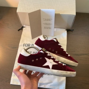 Golden Goose skor - Vinröda Golden Goose Superstar skor i extremt bra skick (9.9/10 ish). Vid köp ingår Originalboxen, originaldustbags och ett bevis på äktenhet (också originelt såklart). Storlek 39. Slitningar är del av design. Nypris är över 4000 kr, vårat-2699. 