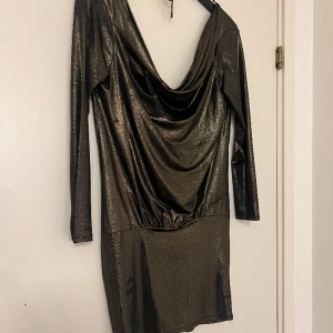 Glammig klänning - Glansig guld-/svartskimrande klänning. Draperad fram, djup urringning i ryggen.