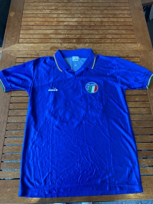 Italien fotbollströja (retro) - Detta är Italiens hemmatröja som användes mellan åren 86-90, denna är troligtvis ifrån 90-talet. Den är gjord i Italien och är gjord av Italienska Diadora. På ryggen har den nr 15 som Baggio hade 1990. Mått: nacke till mudd: 72 cm, armhåla-armhåla 49 cm.