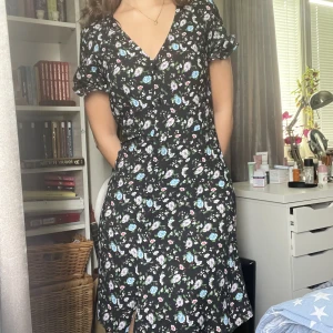 Svart blommig klänning - Jättefin och somrig svart klänning med blommönster i flera färger från H&M, i storlek XS. Klänningen når strax över knäna på mig som är 165 cm lång. Knappt använd och i gott skick. 