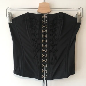 Strapless Korsett  - Korsett utan band med hakar fram och snörning bak. Köpt secondhand.