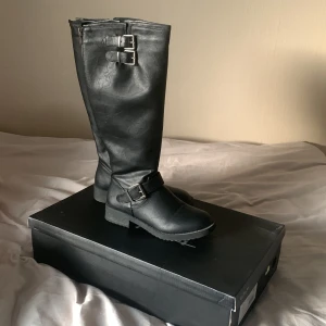 Svarta stövlar - Säljer dessa svarta stövlar i fejk läder och med silver spännen. Använda fåtal gånger men tyvärr finns det små repor,annars i fint skick! Säljs då de inte är min stil längre, skriv för fler bilder! Nypris: 499kr