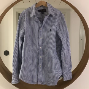 Ralph Lauren skjorta  - Blå, vit randig Ralph lauren skjorta. Skick 9/10. Den har bara används några få gånger. Den säljs för att den blivit för liten. Skriv om du har fler frågor. Pris går att diskutera
