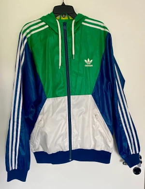 Vintage Adidas vindjacka stl M - Vintage Adidas  windbreaker jacka med luva i bra skick ock med mycket detaljer! Snöret saknar ena metalldekorationen.