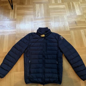 Parajumper jacka  - En marinblå parajumper i mycket gott skick. Den är varsamt använd 8/10 i skick! Den har ett hål på vänsterarmen som är igensatt med en lapp (se bild 3)