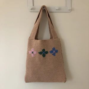 Virkad kasse - Virkad kasse med blommor på i blått, grönt och rosa. Virkat i bomullsgarn och bra kvalitet. Har även ett innertyg.