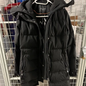 Hollies Subway Dunjacka - En fin dunjacka från Hollies i modellen Subway. Det finns även en svart avtagbar fuskpäls som medföljer i affären. Använd men fin i skicket.