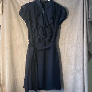 Fröken Söt-klänning  - Jättesöt Fröken Söt-klänning i marinblått, till knäna.  Transparenta armar och kråsvolanger och knappar fram. Knytskärp i midjan. Strl Medium