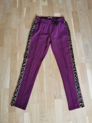 Vinröda konstymbyxor från Scotch and Soda - Ursnygga vinröda konstymbyxor med leopardmönster på sidorna. Färgen syns bäst på sista bilden. Har snörning i midjan och sidofickor. Knappt använda, nyskick!  Storlek: midja: 33 cm och innebenslängd: 73 cm.   63% viskos, 33% nylon-polyamid och 4% elastan.