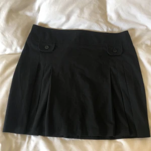 Svart veckad minikjol strl 42 - Minikjol från Lindex i gott skick. Dekorativa fickor å dragkedja där bak. Midjemått på 84cm å 45 cm lång. Köparen står för frakt och Dma gärna vid frågor eller funderingar!