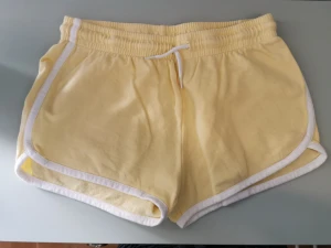 Ljusgula mjukissjorts - Härligt ljusgula mjukisshorts med snörning som är i fint skick! Färgen syns bäst på sista bilden. 100% bomull.