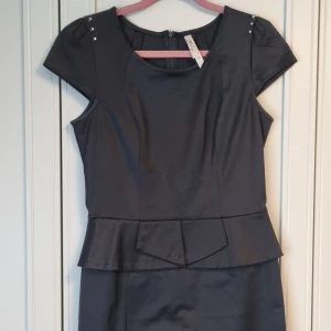 Svart klänning m volangkjol - Svart klassisk knäkort fodral klänning med volang på kjoldelen, små nitar på axlarna. 