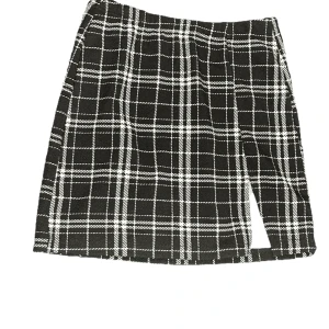 Gullig svart kjol med rutor mönster - Jättefin svart kjol med vitt rutat mönster! Ganska kort och har ett snitt fram.