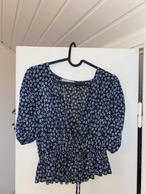 Blommig blus - Blommig blå blus som har storleken M. Tunt silkes tyg som är luftigt.