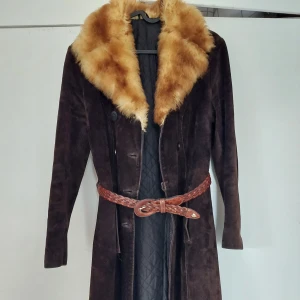 Mockakappa med pälskrage - Den perfekta 70-tals/hippie/boho chic-kappan! Figurnära med raka ärmar, lätt utställd, knälång (på 170 cm) och markerad midja. Mockan har några små vattenfläckar på ärmarna och ett par knappar behöver sys fast bättre, annars toppskick för vintage. Ca S/M.