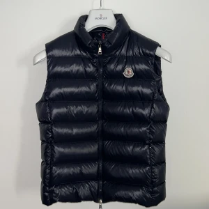 Moncler väst blå - En fin och trendog Moncler väst i marinblå i storlek 1. Den har nästan aldrig använts - i jätte bra skick. Har även lapparna pch kvittot kvar.  Köpt för 5195kr. Köparen står för frakten, kan även mötas upp i Stockholm.