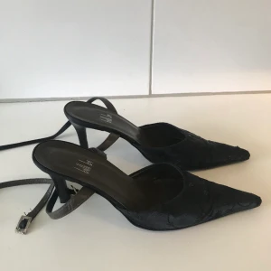 Klackskor från Billi Bi - Svarta pumps med öppen häl och rem, 70mm smal klack, ytterst lite använda. Från Billi Bi Ursprungspris 1000