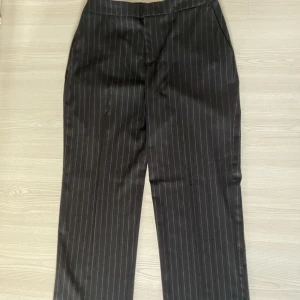 Svarta kostymbyxor  - Ett par medelhög midjade raka kostymbyxor med vita smala ränder. Säljer för att de är för korta i benen till mig( 173 cm). Stl syns inte längre men jag är en M mestadels och de är på gränsen utöver längden också. Midjemått: 75 cm, innerbenslängd: 76 cm. 