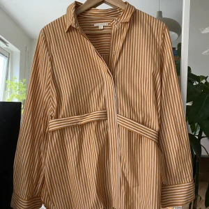 Randig krispig COS blus - Säljer min fina blus/skjorta då den aldrig kommit till användning. Använd max 5 gånger. Vit och orange randig med en ”knytning” runt ryggen. 