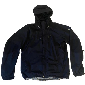 Marmot Regn-och vindjacka M - Svinfet jacka från friluftsmärket Marmot, den är helt vind- och vattentät och har många funktioner som avtagbar och justerbar luva, dragkedjor vid armhålorna, vattentäta dragkedjor, flera funktionella fickor. Perfekt för vandring eller att se mysterisk ut