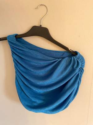 En fin blå oneshoulder topp köpt från ett UF företag. Storlek S. Har en fläck (bild 3). 