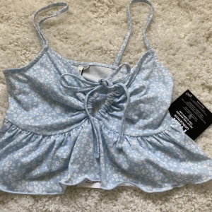 Blommig topp - Säljer denna blå vit blommiga söta topp med knyte där fram💗den har även en lite volang nedtill💗aldrig använd, prislapp kvar  Nypris 139   Frakt tillkommer 💗