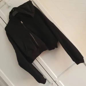 Träningsjacka - Svart, mjuk, träningsjacka med luva och blixtlås. Kort i modellen. Aldrig använd. 