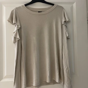 Tröja - Långärmad tröja med volanger i axlarna som är öppen vid volangerna. I mycket gott skick 