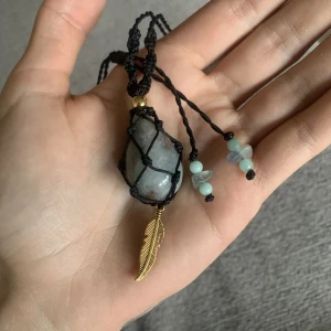Akvamarin halsband - Akvamarin sten 3,5cm X 2cm ”droppe” med en guldfjäder i rostfritt stål med guldfärg under stenen. Över stenen är en guldpläterad pärla i rostfritt stål. 4st små akvamarinpärlor och 2st blå kalcitstenar i ändarna. Ställbar i storlek, vattentålig. Makramé