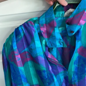 Blus  - Skimrande blus med armpuffar och knappar runt halsen. Storlek 42 