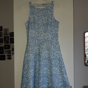 Blommig klänning - Klänning i fint blåblommigt mönste med delvis öppen rygg. Den är endast använd ett fåtal gånger och i jättebra skick. 