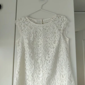 Vit blus/linne - Jättefint vitt linne med spetsmönster och guldfärgad knapp baktill. Inga fläckar eller skador och i mycket gott skick.