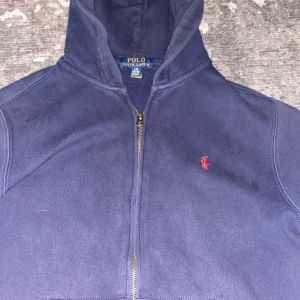Ralph Lauren zip hoodie - Tröjan sitter väldigt bra och tröjan passar till 12/13 åringar tröjan har ett sköntmaterial och är snygg på tröjan är mörkblå.