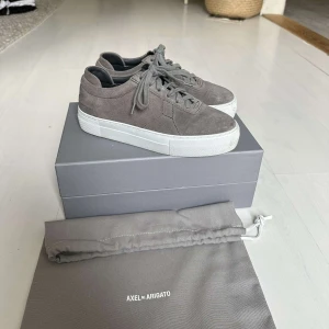 Axel Arigato skor  - Axel Arigato skor, mörkgråa i mocka. Nyss köpta och använda Max 5 gånger, ser ut som nya. Det är storlek 36. Pris när jag köpte 2100kr, säljer för 1400+frakt.  Påse och kartong kommer med! 