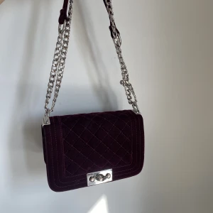 Vinröd väska  - Mörkröd vinröd axelremsväska / handväska i sammetliknande material med silverkedja. Superfin och bra skick, ett litet innerfack finns.