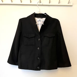 HOPE kavaj/jacka - Svart kort kavaj/jacka från HOPE. Mjuk och skön ull. Croppad ärm. Använd inomhus som en skön kavaj på vintern och ute som en tunn jacka på sommaren. Sparsamt använd. Storlek 38. Jag är stl 36 och tycker den passar perfekt