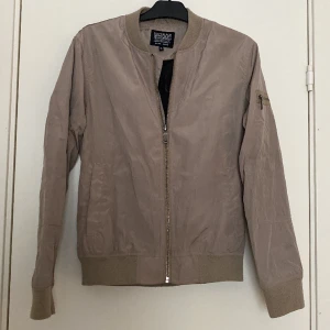 Jacka - Bomberjacka i en mörk beige färg i använt skick
