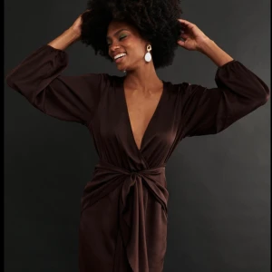 Satinbrun kort klänning med ballongarm  - Super snygg brunsatinklänning med ballong arm och knyt detalj vid midjan. Väldigt bra skick andvänd 1 gång. 