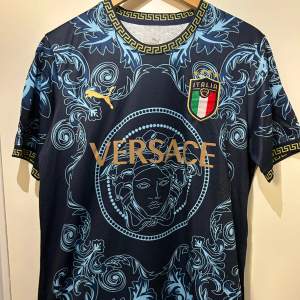 Mörkblå Italien X Versace T-shirt med Versace loggor runtom och guldiga detaljer samt text. Helt ny med etikett i storlek M.