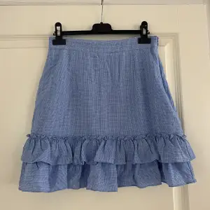 Blå finare kjol från Nakd. Mycket sparsamt använd, därav fortfarande i väldigt fint skick! Kjolen har en dragkedja på sidan och är i ett rutigt mönster.  Midjemått: ca 70 cm