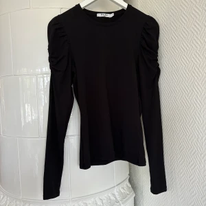 Topp - Svart långarmad topp från NA-KD, fina detaljer vid axlarna som ger lite volym men ändå diskret 🖤