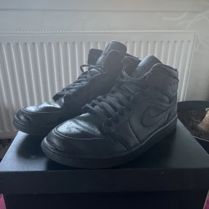 Jordan 1 Mid Triple Black / Svart 46 - Säljer mina Storlek 46 Jordan 1 Triple black Mids nu för har slutat använda de. Skorna är i mycket bra skick och sällan använda. Har pyttelite creasing men annars i nyskick. Originallådan ingår.