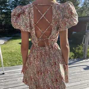 Sommarklänning - Sommarklänning i blommigt mönster med puffiga armar och knyte i ryggen! 🌸Köpt från NA-KD och använd sällan. Storlek 34 men då det är knyte i ryggen går det att göra större. Inga defekter.